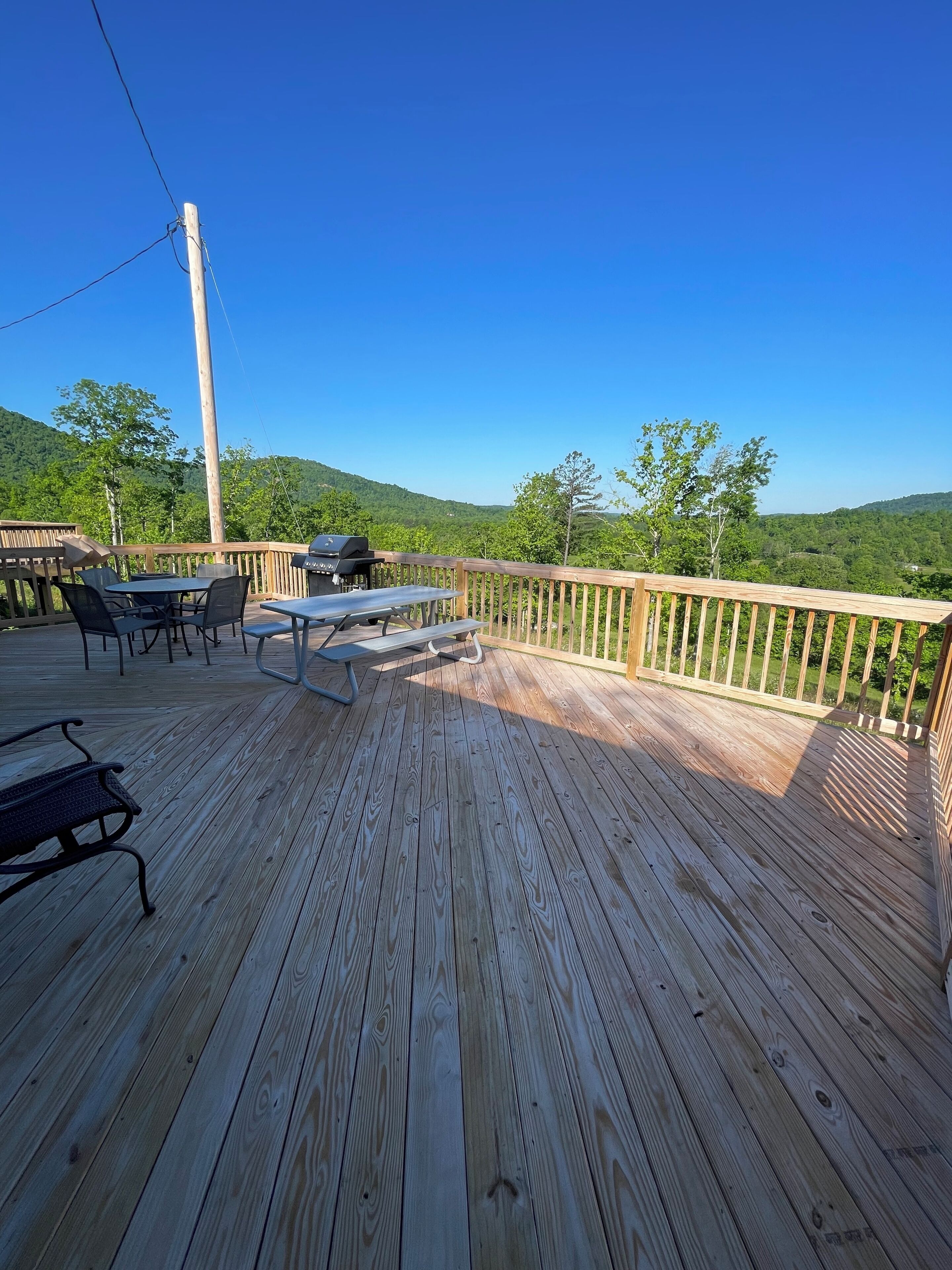 A wooden deck with outdoor seating, a grill, and a view of green hills.