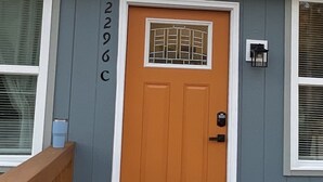 A single-story building with a wooden deck, a brown door with a window, and a mailbox.