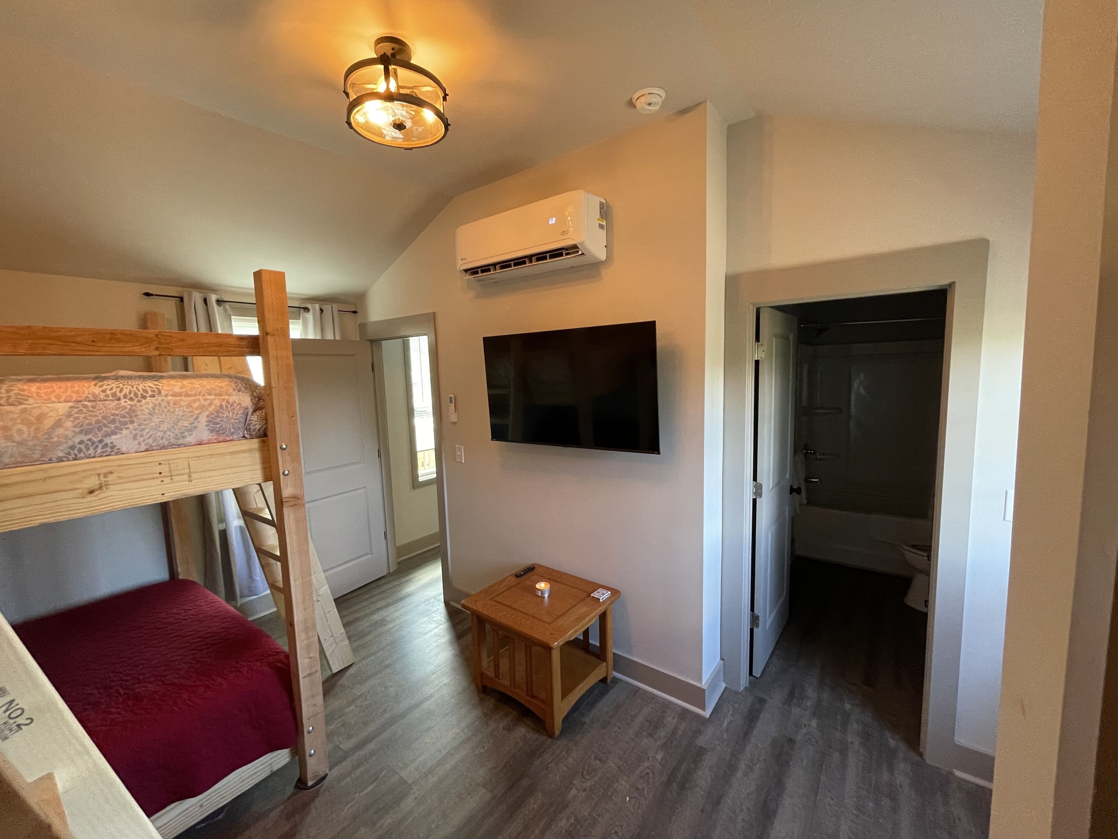 A room with a bunk bed, a small wooden table, a mounted TV, and an air conditioning unit.