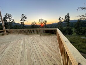 Una terraza de madera con barandilla, con vistas a un paisaje pintoresco con árboles y una puesta de sol.