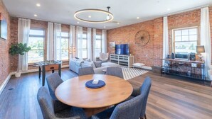 A spacious room with a round wooden table, grey upholstered chairs, a foosball table, a sofa, and a television. - Historic Main Street Lofts - 3rd floor (Gunnison)