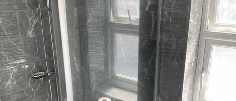 A modern bathroom with a glass-enclosed shower, a toilet, and a window providing natural light.