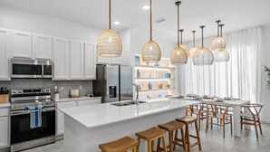 Una cocina moderna con armarios blancos, electrodomésticos de acero inoxidable y una isla central con taburetes de bar.