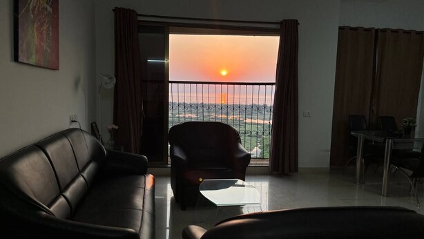 Ein Wohnzimmer mit Sofa, Sessel und Tisch. Ein Balkon bietet Blick auf den Sonnenuntergang.