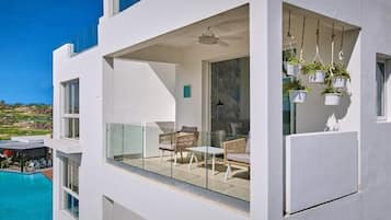 A modern building with a glass balcony, outdoor seating, and hanging planters.