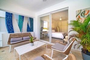 A modern hotel room with a balcony, a sofa, a dining table, and a large window. - Cana Brava Residences Rental Apartment  (Punta Cana)