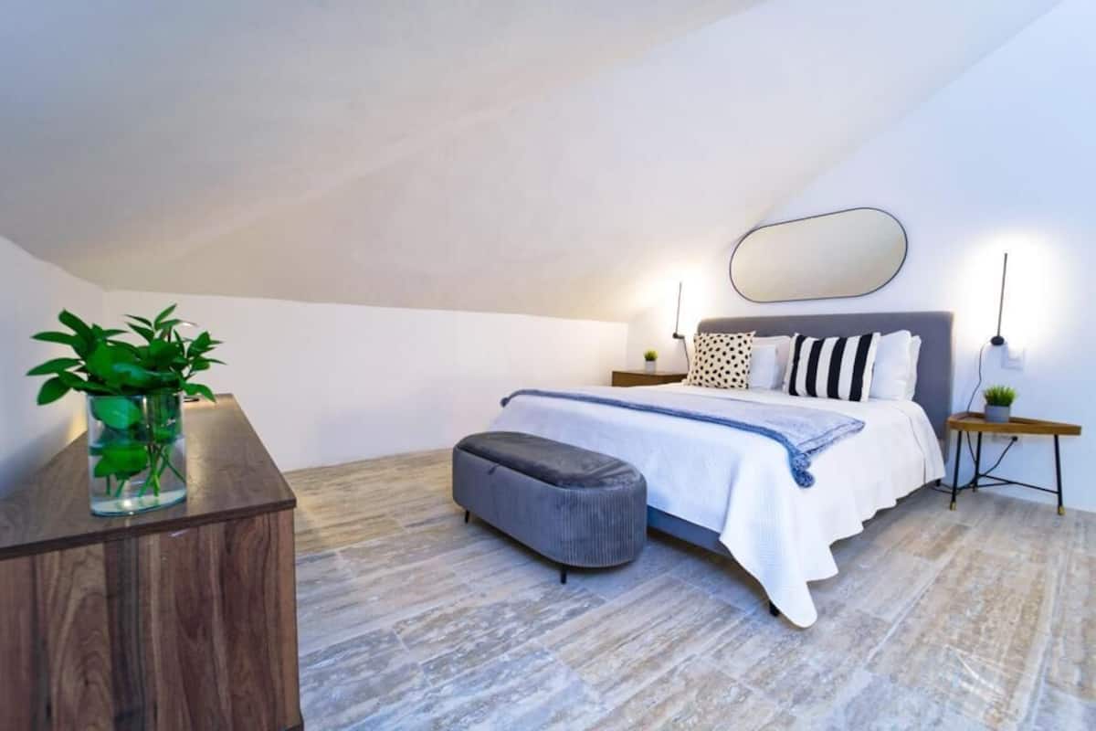 A bedroom with a bed, bedside tables, a mirror, and a potted plant.