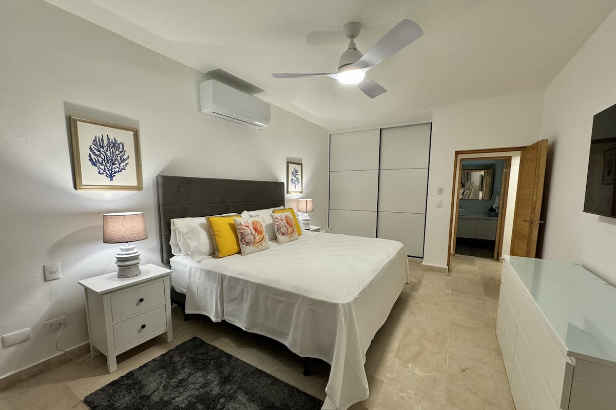 A bedroom with a bed, bedside tables, a ceiling fan, and a black rug.