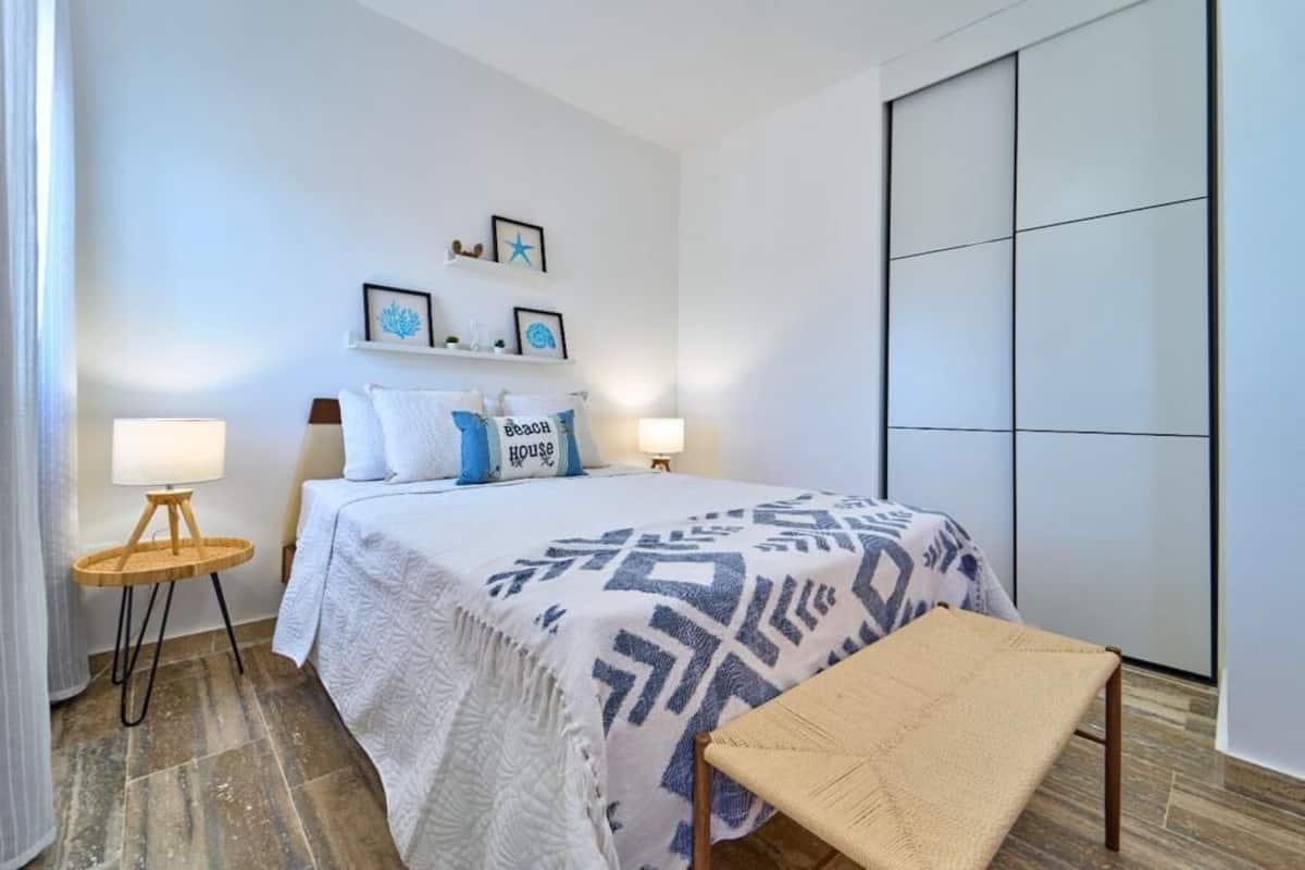A bedroom with a bed, bedside lamps, a bench, and wall decorations.