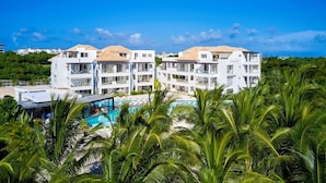 A resort with multiple white buildings, a swimming pool, and lush greenery. - Cana Brava Residences Rental Apartment  (Punta Cana)