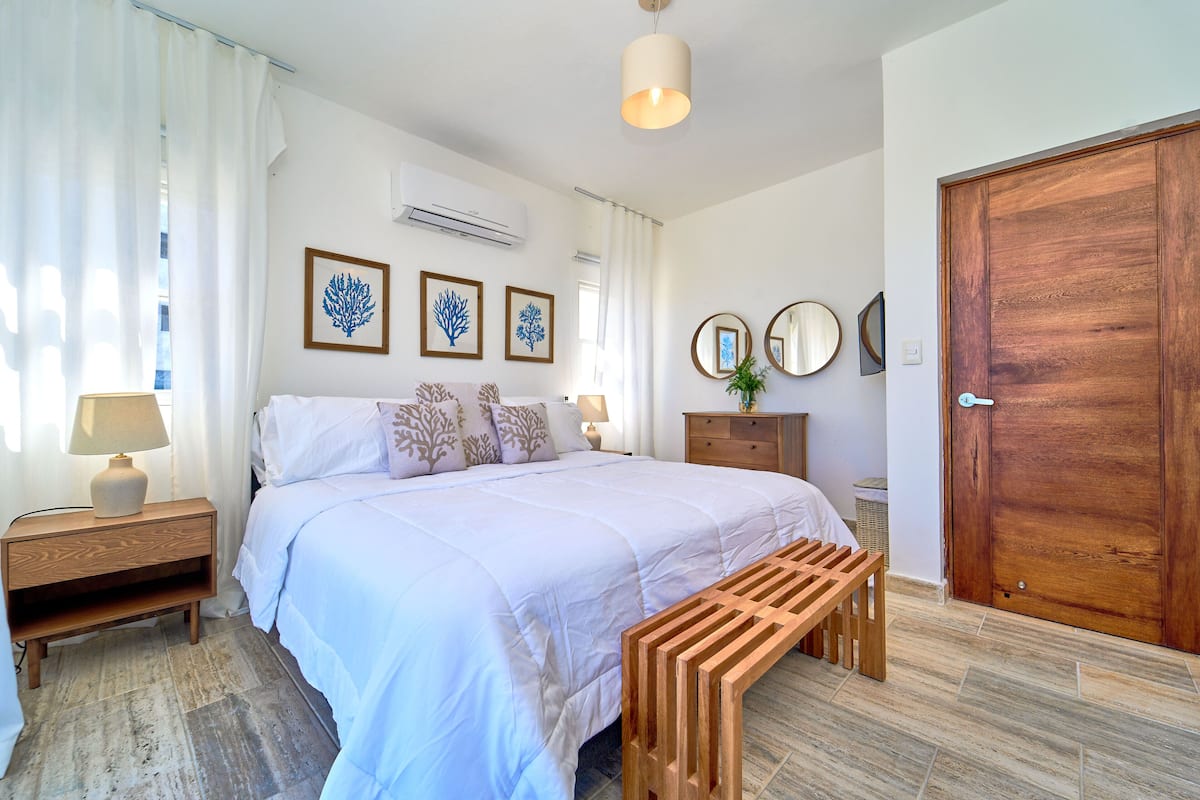 A bedroom with a large bed, wooden nightstand, bedside table, and a bench.