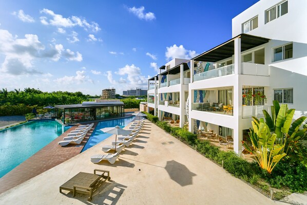 A modern hotel with a pool, sun loungers, and a view of the city skyline. - Cana Brava Residences Rental Apartment  (Punta Cana)
