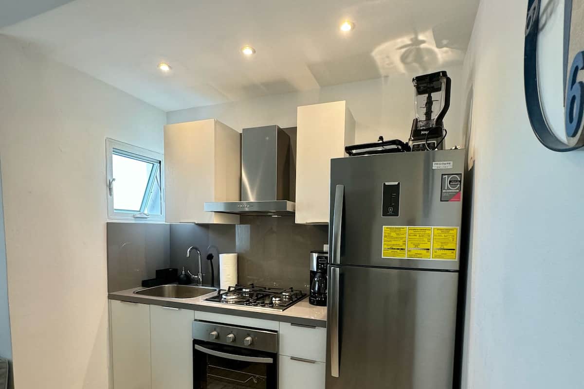 A compact kitchen with a gas stove, oven, stainless steel refrigerator, and a window above the sink.
