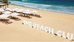 A beach with lounge chairs and umbrellas, and the words "THE BEACH CLUB" written on the sand. - Cana Brava Residences Rental Apartment  (Punta Cana)