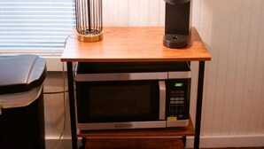 A kitchen area with a microwave, a Keurig coffee maker, and a lamp on a wooden table. - Boutique Beeville Cottage (Beeville)