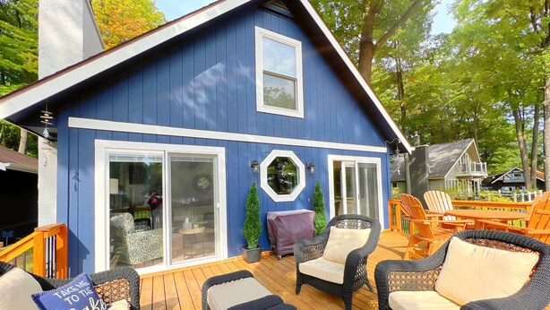 A blue house with a deck, outdoor seating, and a large window.