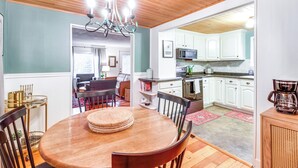 Un'area pranzo con tavolo e sedie in legno, un lampadario e una cucina con pensili bianchi e un forno a microonde.