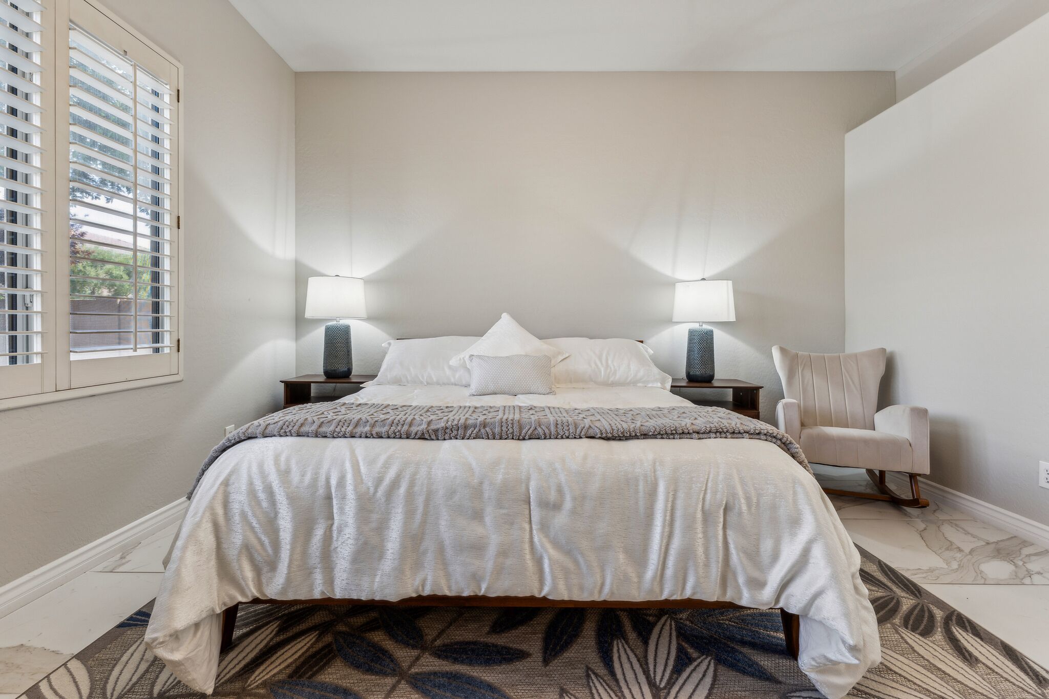 Une chambre à coucher bien rangée, avec un grand lit, deux lampes de chevet, une chaise et un tapis à motifs.