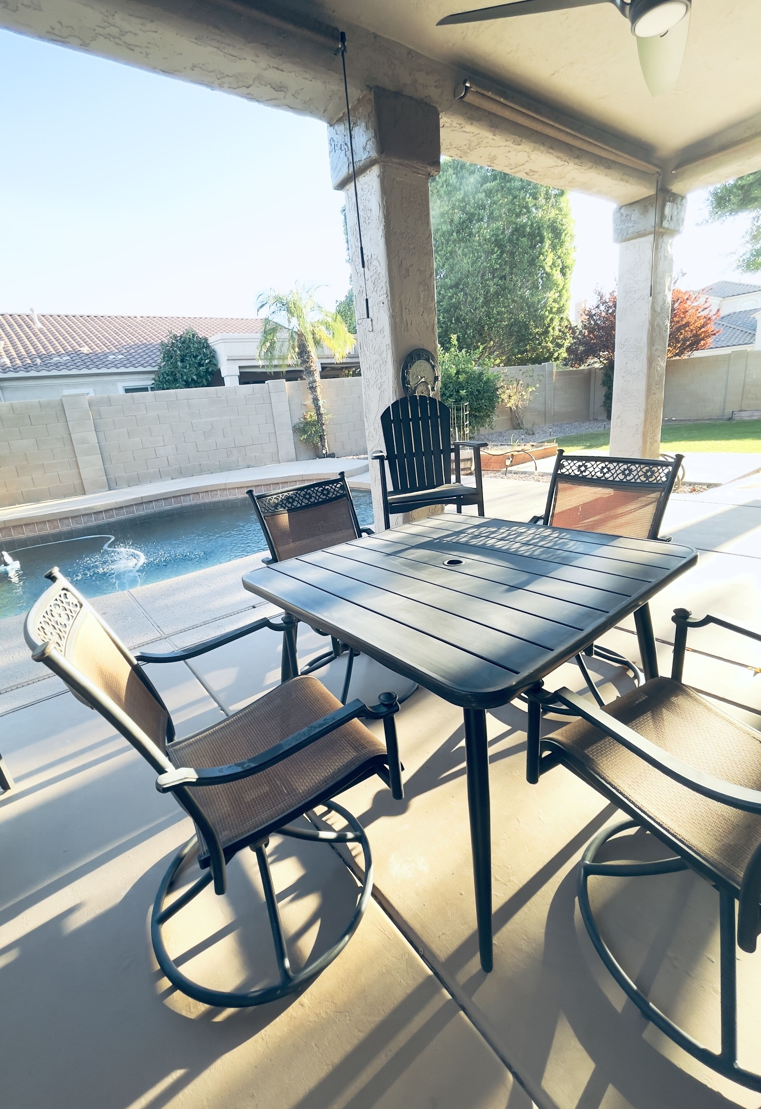 Een terras buiten met een tafel en stoelen, een zwembad en uitzicht op een woonwijk.