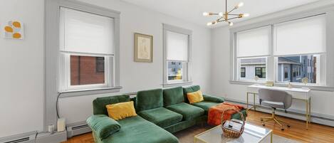 A modern living room with a sectional sofa, a desk, and a large window.