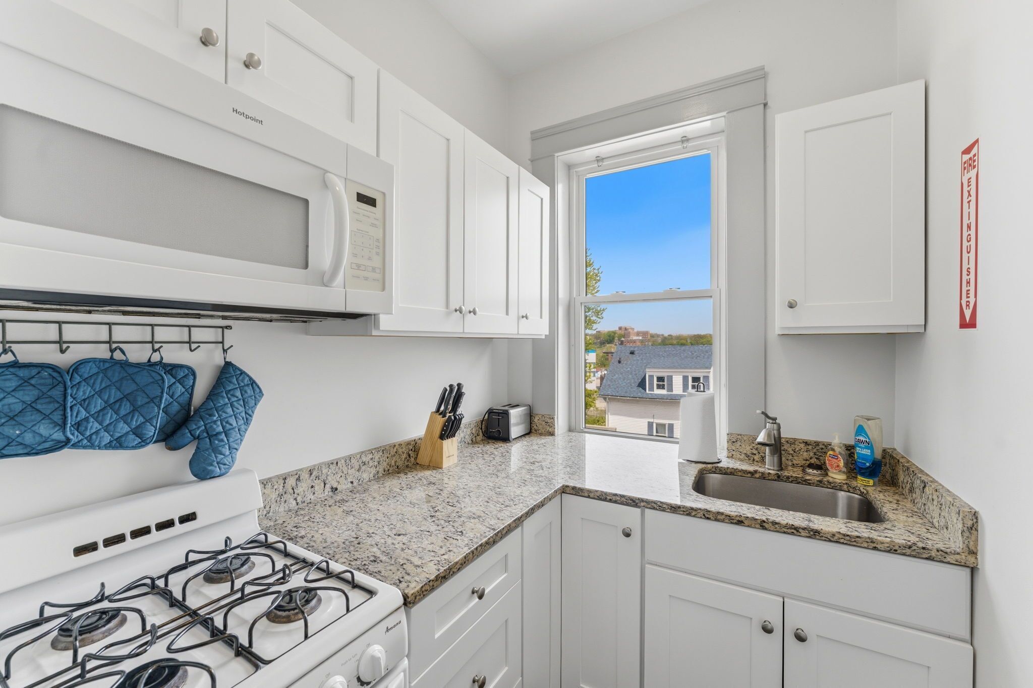A modern kitchen with white cabinets, a gas stove, a microwave, and a window with a view of houses.