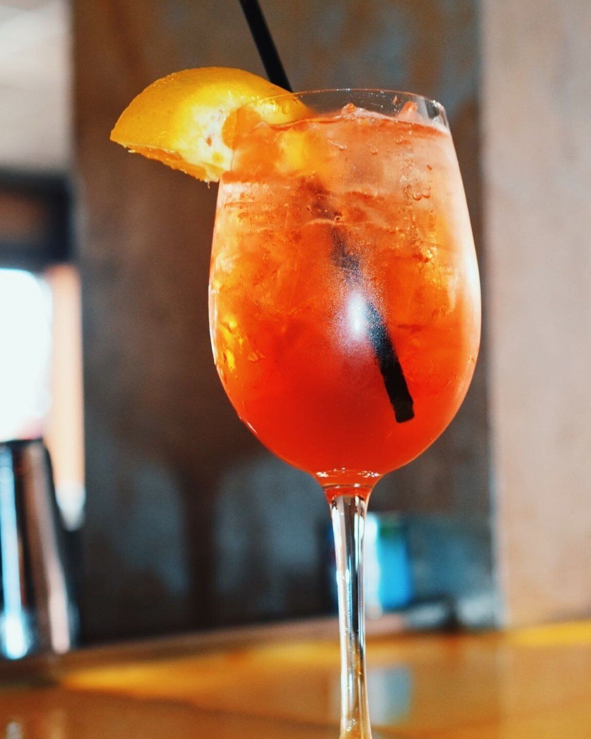 A cocktail glass with a lemon garnish and a straw, placed on a wooden surface.