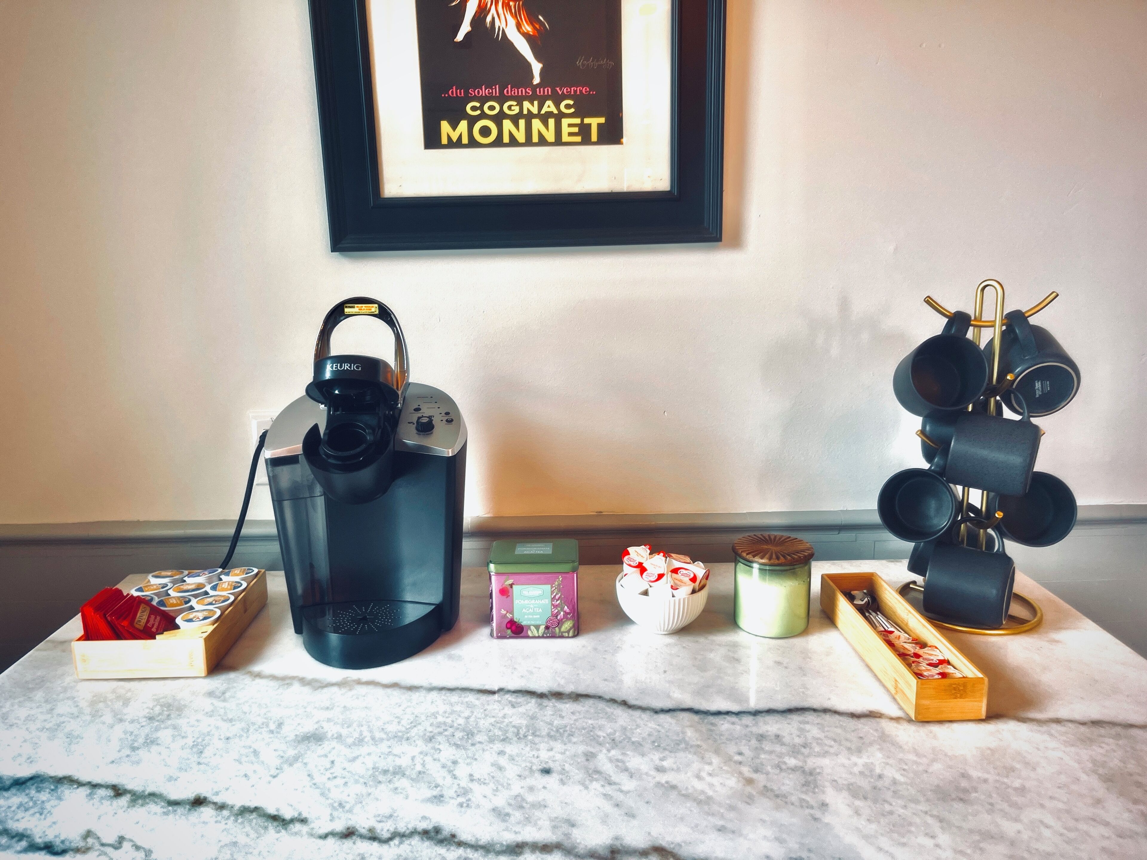 Une machine à café, un porte-tasses et divers dosettes de café sur un comptoir en marbre.