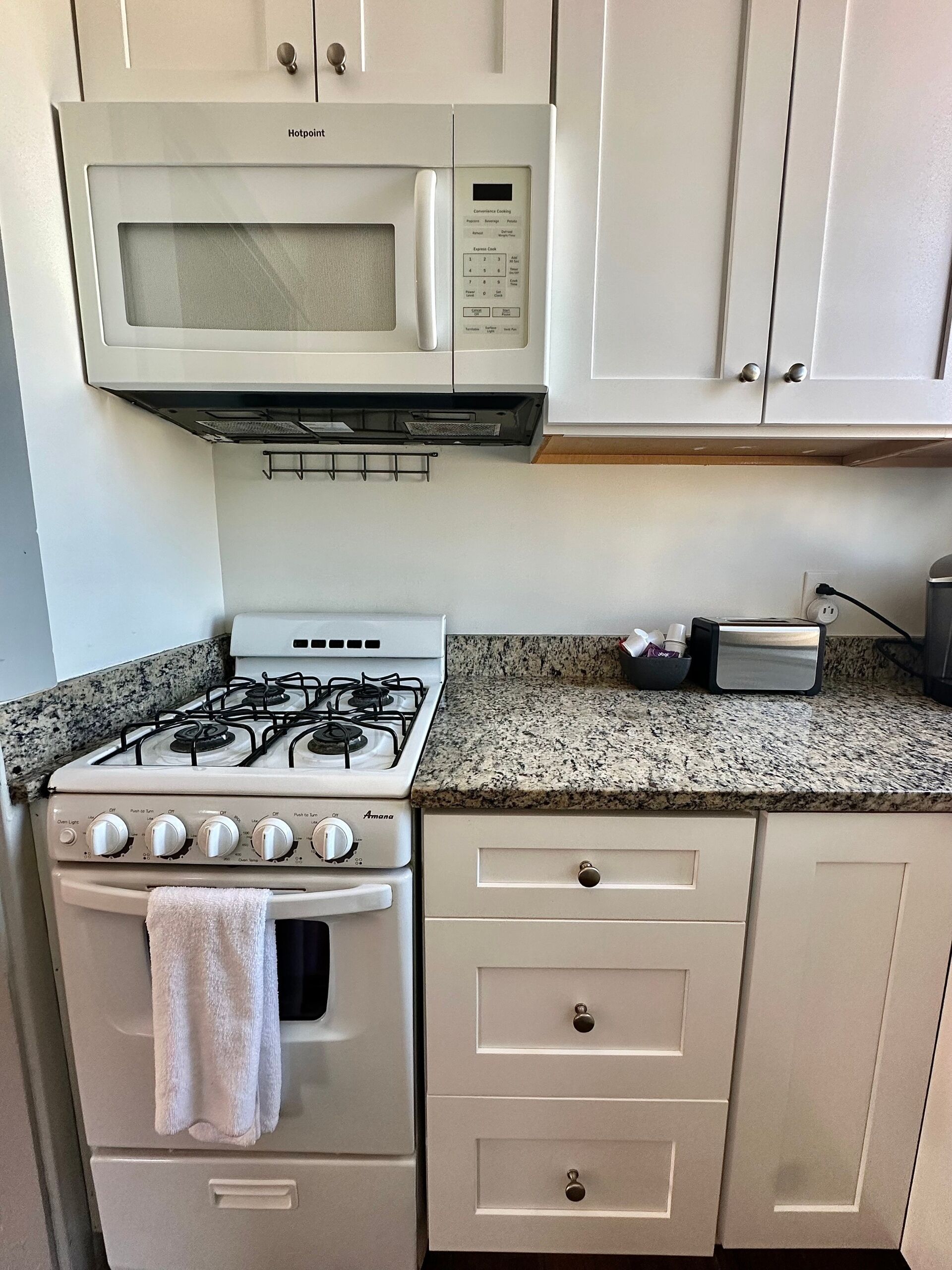 A kitchen with a stove, oven, microwave, granite countertop, and white cabinets.