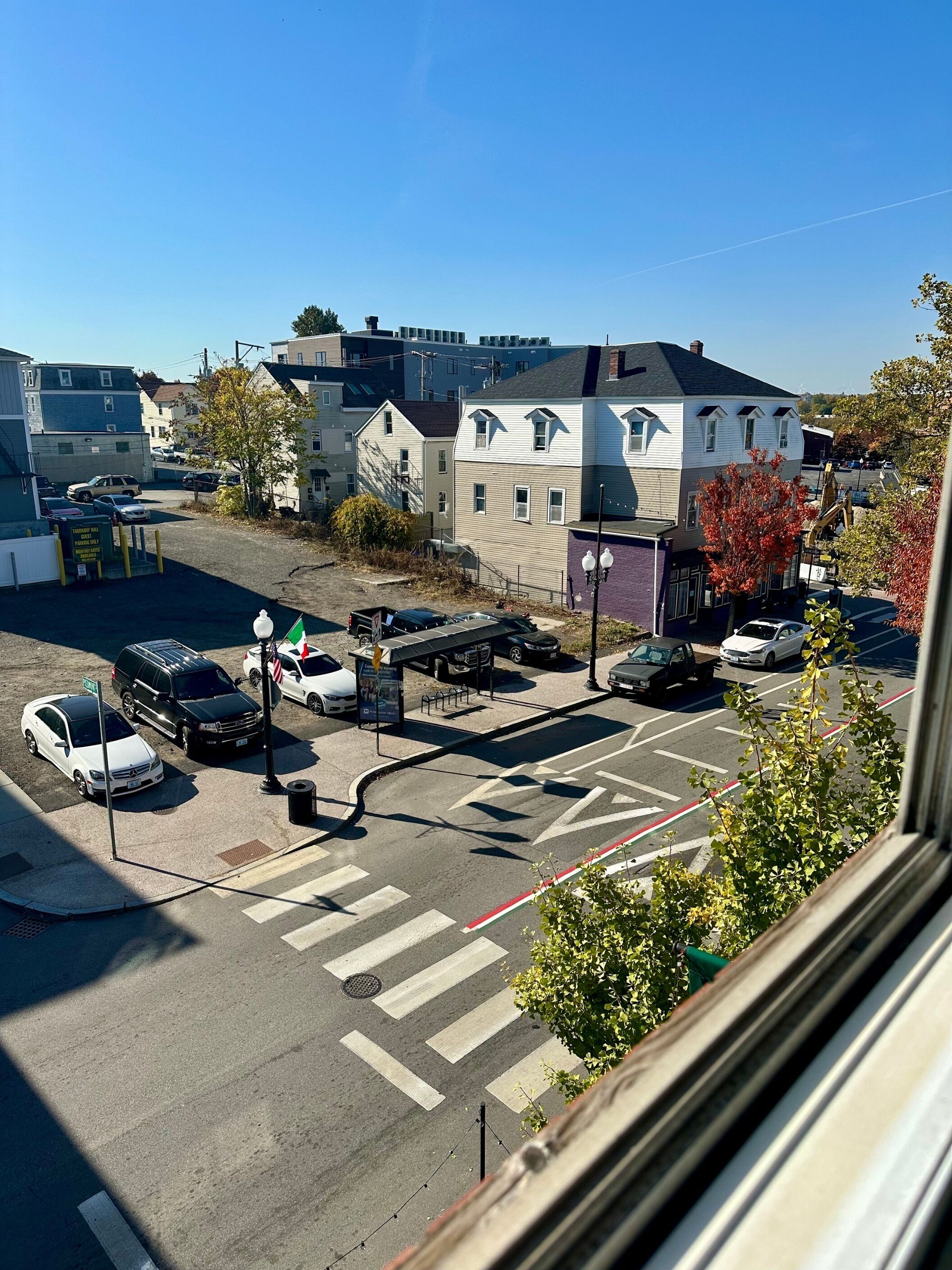 Vista de la calle con coches aparcados, un paso de peatones y edificios al fondo.