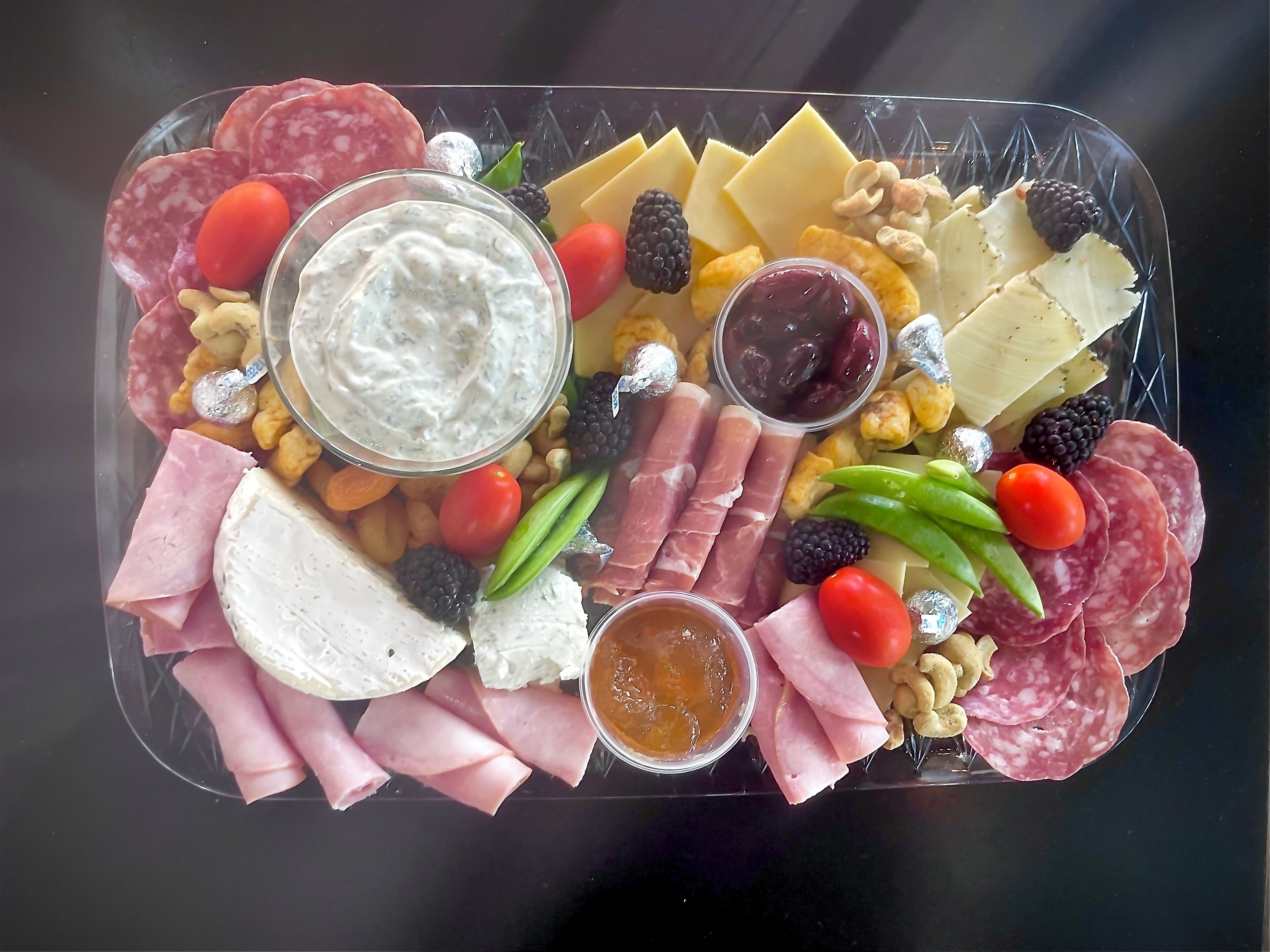 A charcuterie board with various meats, cheeses, fruits, and dips.