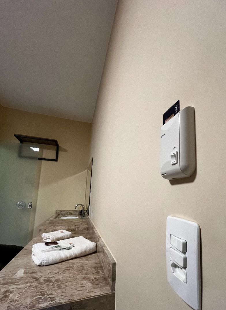 A bathroom with a marble countertop, a towel rack, a mirror, and a wall-mounted soap dispenser.