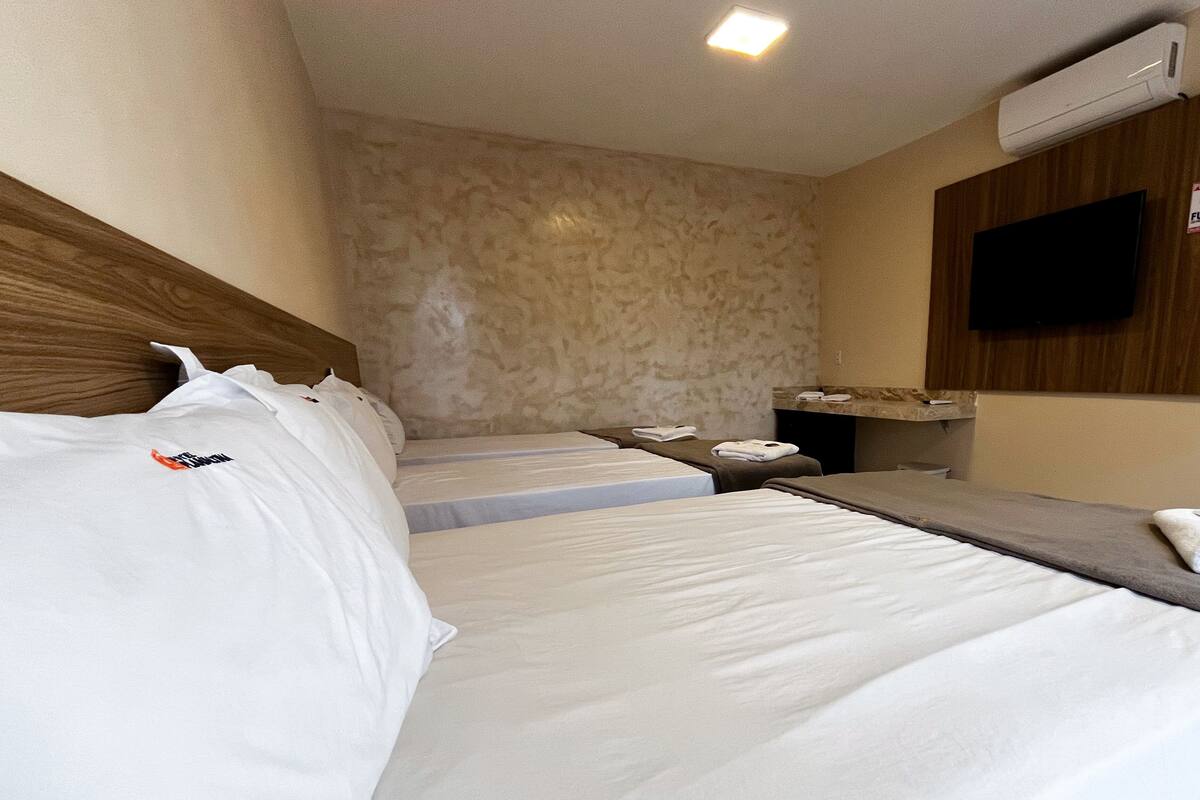 Habitación de hotel con tres camas, un televisor de pantalla plana montado en la pared y un aire acondicionado.