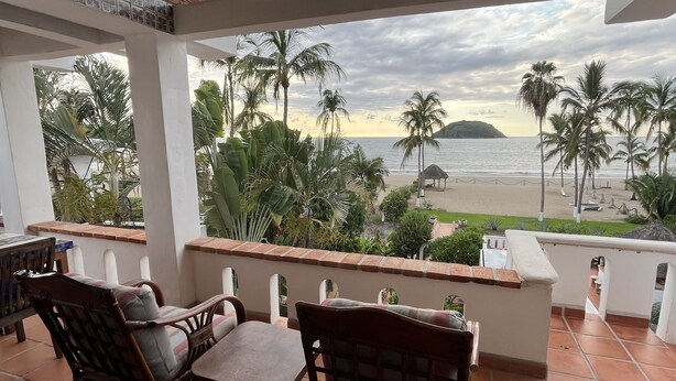 A covered outdoor seating area with a view of the beach and palm trees. - Oceanfront studio apartment  (Rincón de Guayabitos)