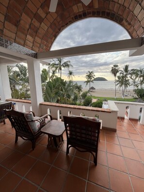 A covered outdoor seating area with a view of the beach and palm trees. - Oceanfront studio apartment  (Rincón de Guayabitos)