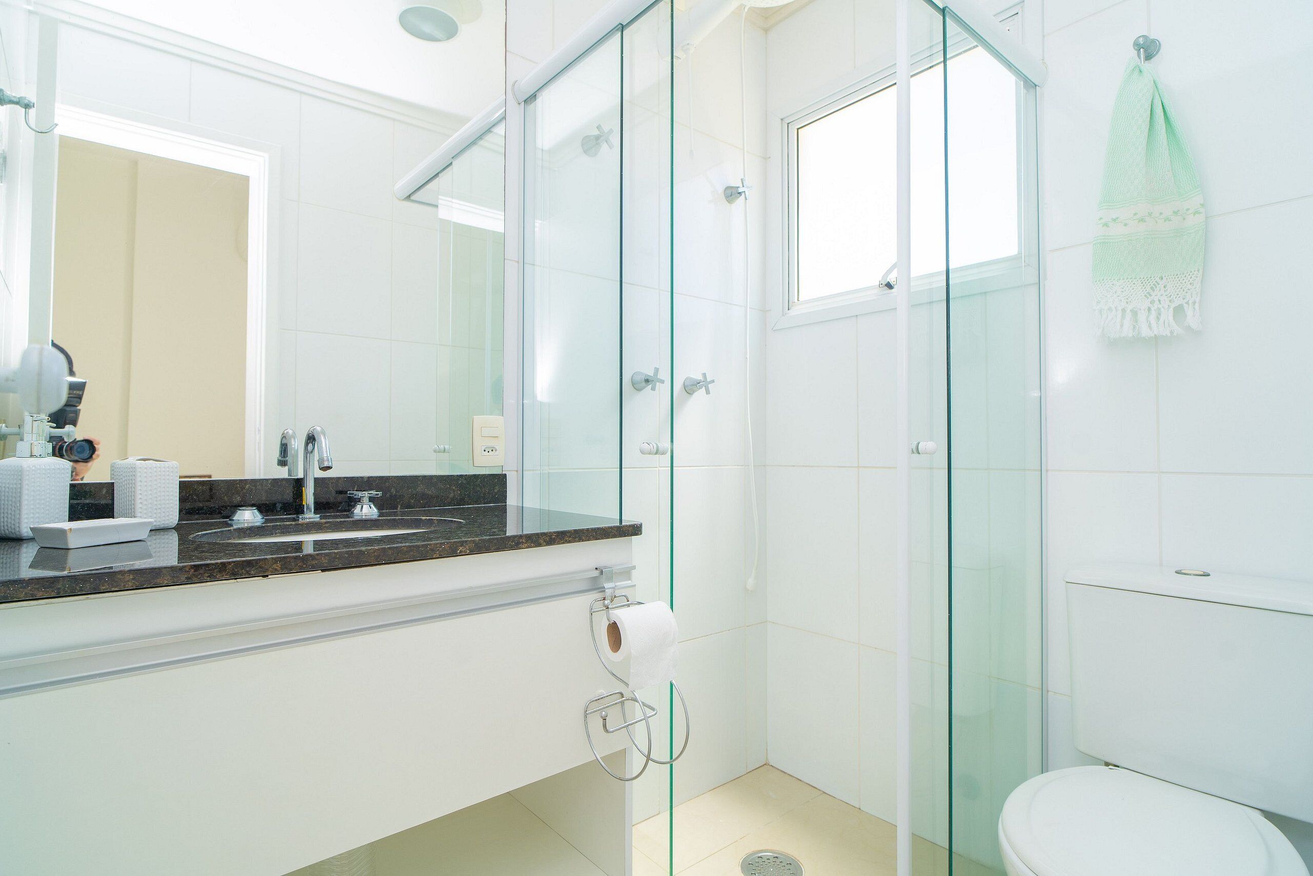 A modern bathroom with a glass shower enclosure, a white toilet, and a sink with a marble countertop.