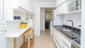 A modern kitchen with white cabinetry, a built-in microwave, and a stainless steel sink. - Elegante Apartamento em Enseada no Guarujá (Guarujá)