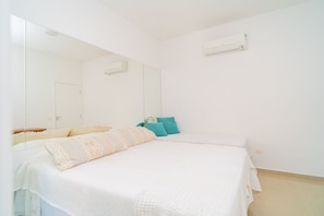 Quarto com cama, espelho, ar condicionado fixado na parede e uma porta.