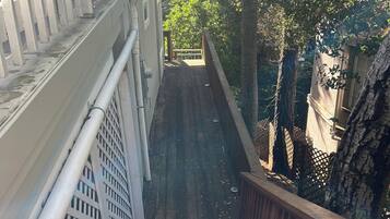 A wooden staircase leading to a balcony with a metal railing, surrounded by trees and a building facade.