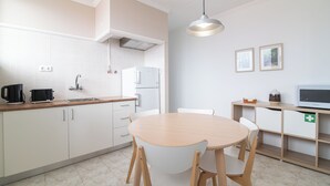 A modern kitchen with white cabinets, a wooden dining table, and a built-in microwave. - Livramento Residence (Ponta Delgada)