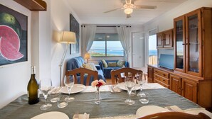 Un comedor con una mesa dispuesta para dos, un televisor y vista al mar.
