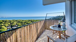 Un balcón con vista al mar, una mesa con vasos y un florero, y una valla de madera.
