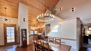 Un vaste espace dédié à la salle à manger, avec une table et des chaises en bois, un lustre, et une vue sur la cuisine et le salon.