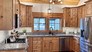 Une cuisine dotée de meubles en bois, de plans de travail en granit, d’appareils électroménagers en acier inoxydable et d’un plafond en bois.