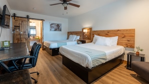 A hotel room with two beds, a desk, a chair, a ceiling fan, and a small table with a plant. - Springs Lodge & Cafe (Hot Springs)