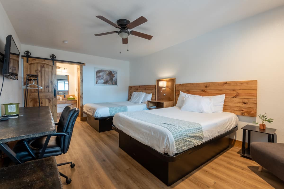 A hotel room with two beds, a desk, a chair, a ceiling fan, and a small table with a plant.