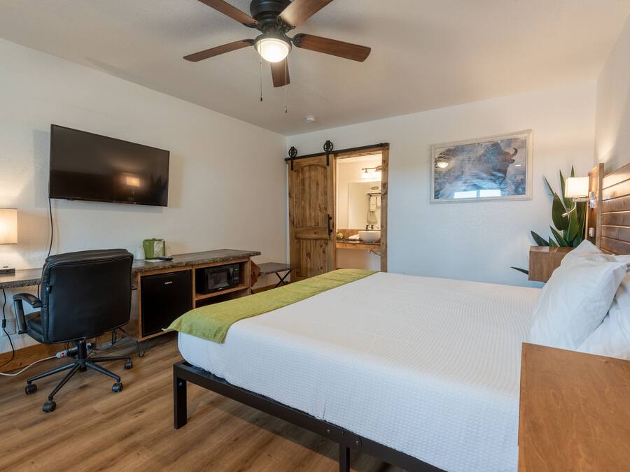 Une chambre d’hôtel équipée d’un lit, d’un bureau, d’une chaise, d’une télévision, d’un ventilateur de plafond et d’une armoire en bois.