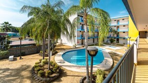 A pool area with palm trees, a building with blue and white exterior, and a clear sky. - Tropical Tranquility - Corcega (Stella)