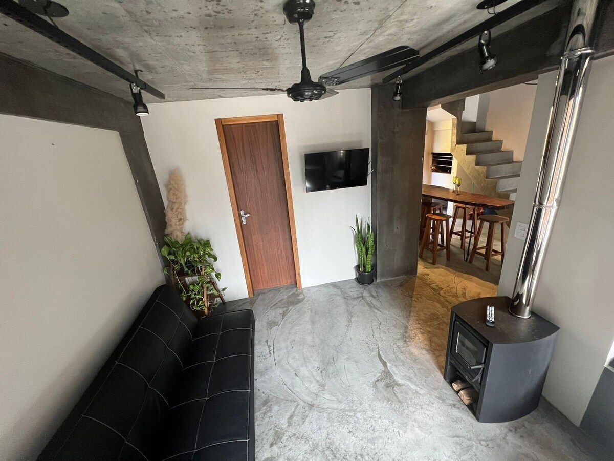 Un salon avec un canapé noir, une cheminée, un téléviseur fixé au mur et un escalier menant à un espace repas.