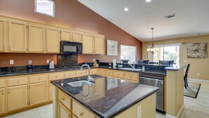 A modern kitchen with beige cabinets, granite countertops, a stainless steel dishwasher, and a large island with a sink. - Resort Perks, Patio & Gas Grill: Indio Retreat! (Indio)