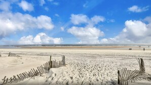 Une vaste plage de sable fin, avec un ciel dégagé et quelques nuages.
